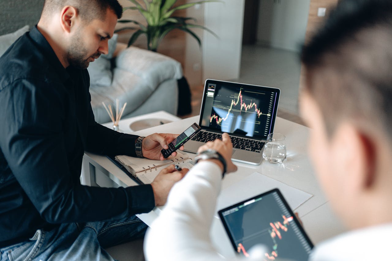 Two businessmen analyzing financial data on laptops in a modern office setting.
